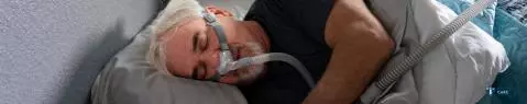 Un homme portant un masque PPC est allongé dans le lit, sur le coté droit.